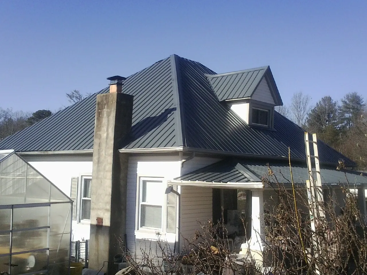Dark blue standing seam metal roof on a white farmhouse with dormer — Slate & Tile Roof Repair by Roofing Brothers in Windom