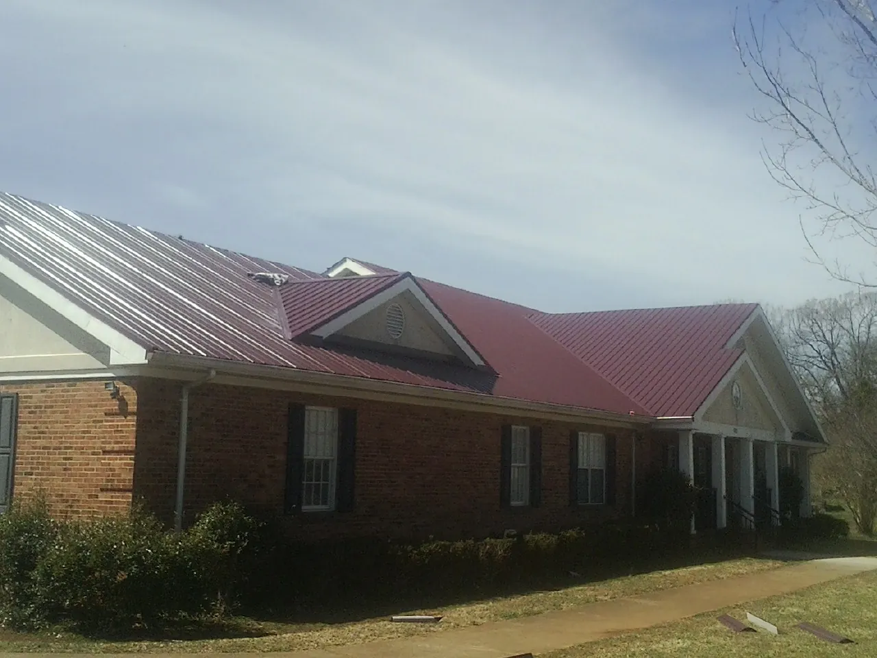Red metal roof with gabled entries on a long brick building, from a Hail Damage Roof Repair job in Windom