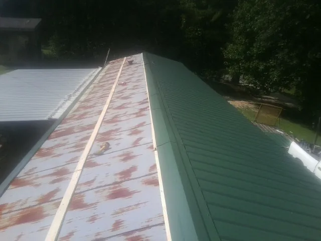Old rusted panels beside newly installed green metal roofing — Wind Damage Roof Repair by Roofing Brothers in Windom