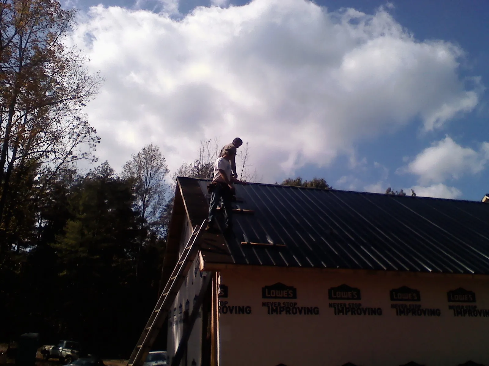 Roofer fastening dark metal panels high against a cloudy sky, from a Roof Inspection job in Windom
