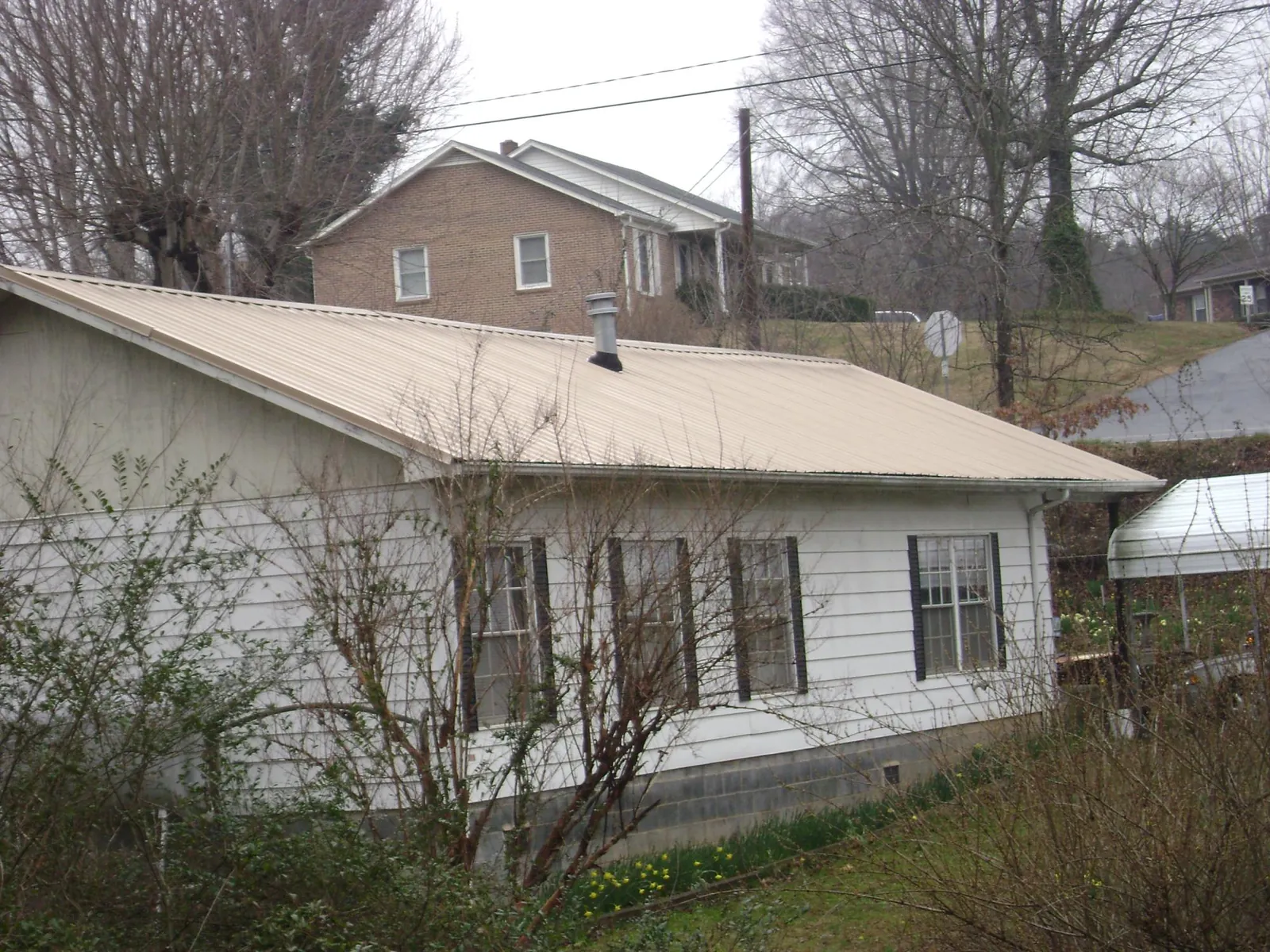 Tan metal roof on a white sided house set into a hillside — Commercial Roofing by Roofing Brothers in Windom
